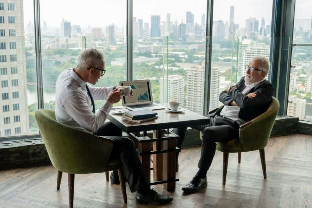 two men sitting at a table talking conspiracy